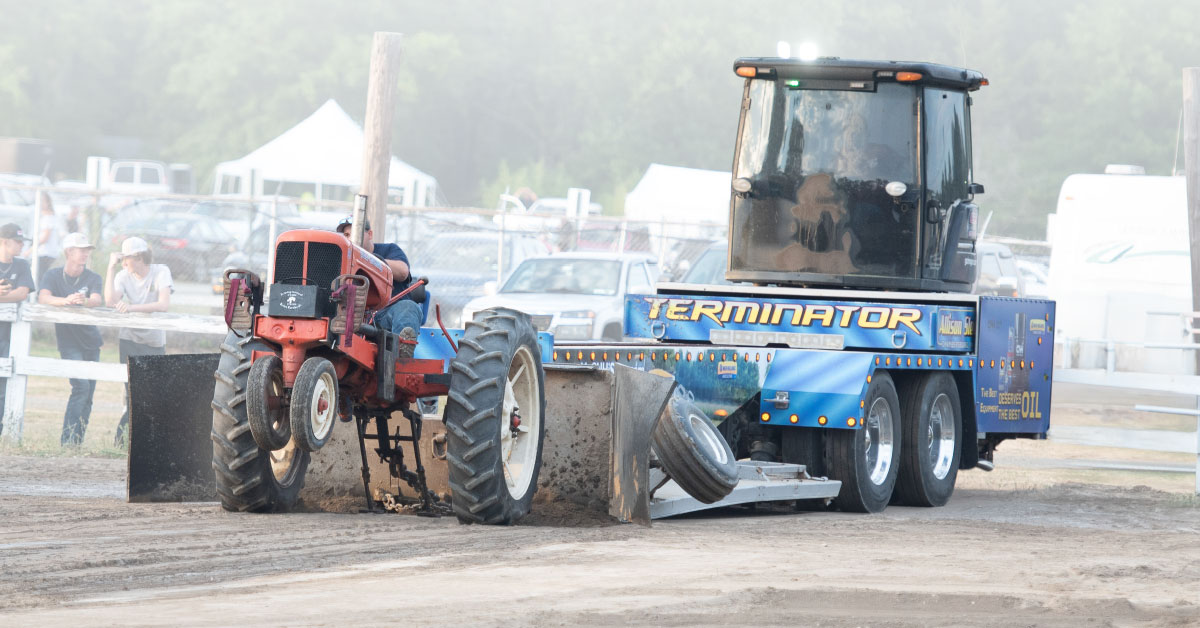 A photo of a tractor pull at the Ulster County Fair. A Farm tractor is pulling another vehicle while a crowd watches.
